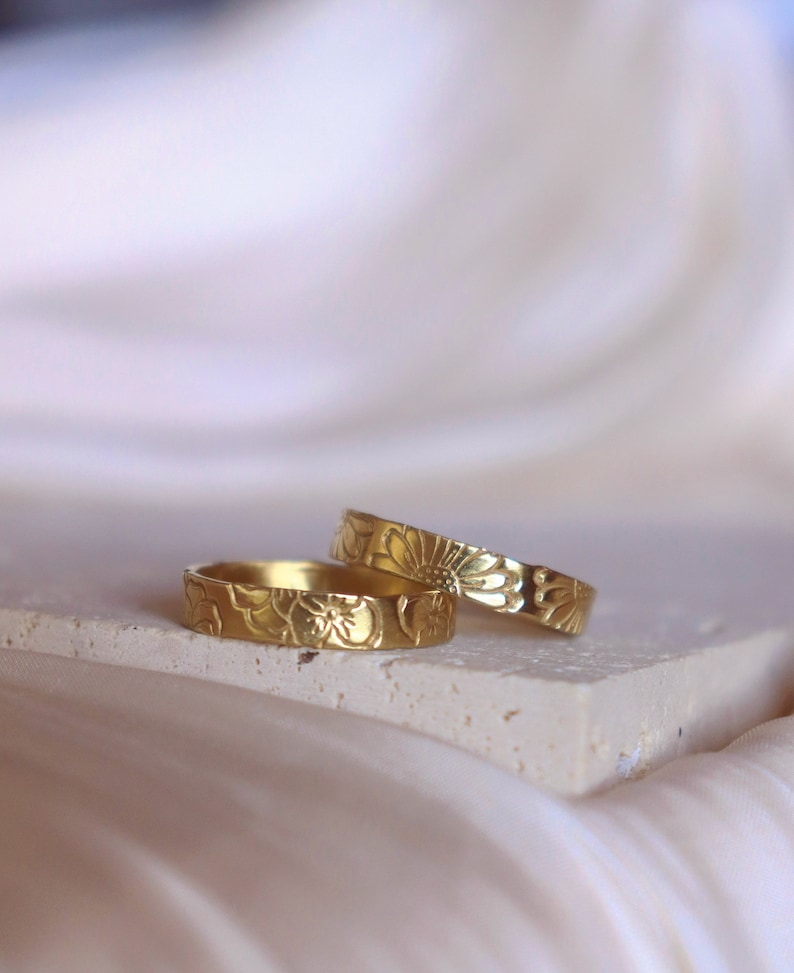 May include: Two gold rings with a floral design. The rings are stacked on top of each other.