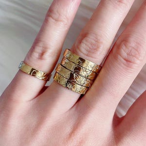 Op de afbeelding: Een set van vijf gouden ringen met een bloemenmotief. De ringen zijn op elkaar gestapeld en worden aan een vinger gedragen.
