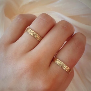May include: Two gold rings with a floral design. The rings are worn on the fingers of a hand.