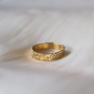Op de afbeelding: Een gouden ring met een bloemenmotief. De ring is gegraveerd met een gedetailleerd patroon van bloemen en bladeren.