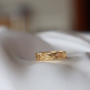 Op de afbeelding: Een gouden bandring met een gedetailleerd bloemenmotief. De ring is gemaakt van massief goud en heeft een delicaat bloemenpatroon.