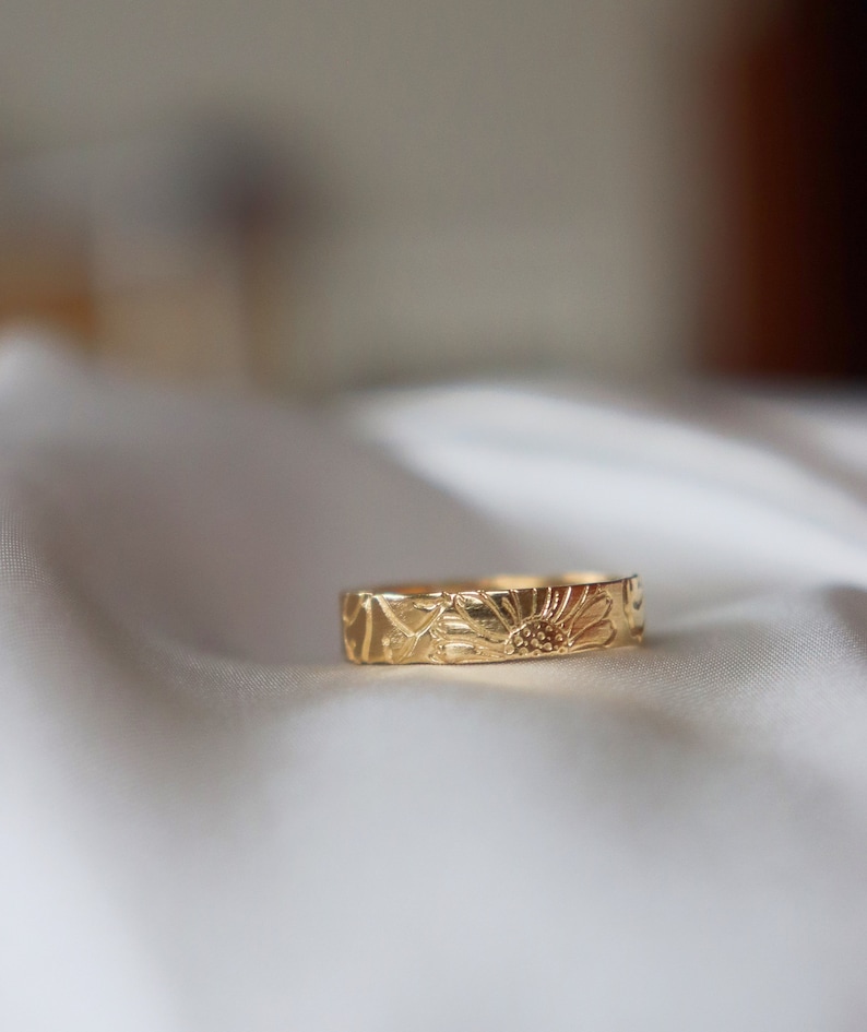 Op de afbeelding: Een gouden bandring met een gedetailleerd bloemenmotief. De ring is gemaakt van massief goud en heeft een delicaat bloemenpatroon.
