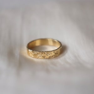 Op de afbeelding: Een gouden bandring met een ingewikkeld bloemmotief gegraveerd rond de hele band.