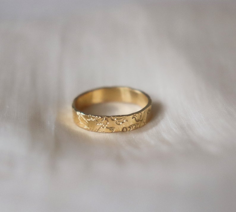 Op de afbeelding: Een gouden bandring met een ingewikkeld bloemmotief gegraveerd rond de hele band.