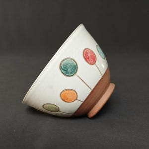 May include: A white ceramic bowl with a brown rim. The bowl is decorated with colorful circles and lines.