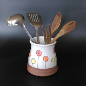 Könnte beinhalten: Weißer Keramik-Utensilienhalter mit braunem Rand und orangefarbenen und gelben Punkten. Der Halter ist mit verschiedenen Küchenutensilien gefüllt, darunter eine Schöpfkelle, ein Schlitzspatel, ein Holzlöffel und eine Gabel.