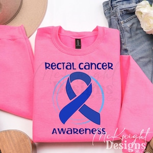 Puede incluir: Sudadera rosa con una cinta azul y el texto "Rectal Cancer Awareness".