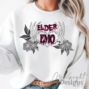 May include: White sweatshirt with a graphic design of two skeletal hands forming a heart shape with the words "ELDER EMO" inside the heart. The graphic is in black and pink.