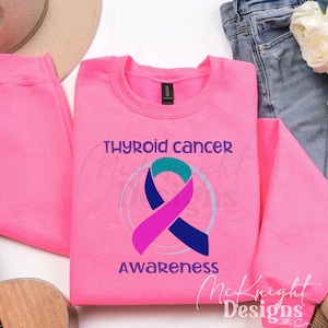 May include: Pink sweatshirt with the text "Thyroid Cancer Awareness" and a teal, pink, and blue ribbon design.