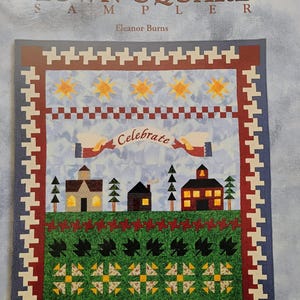 May include: A quilt pattern titled "Town Square Sampler" by Eleanor Burns. The quilt features a red, white, and blue color scheme with a variety of blocks, including a church, a schoolhouse, and a house. The quilt is surrounded by a red and white border.