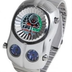 Puede incluir: Un reloj de pulsera plateado con un diseño único. La esfera del reloj presenta una pantalla circular con un diseño negro y verde, y tres esferas más pequeñas. El reloj tiene una pulsera de metal plateado.