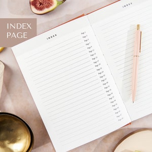 May include: An open notebook with a white cover and lined pages. The notebook has an index page with numbered pages from 1 to 49. A pink pen is lying on the right page of the notebook.