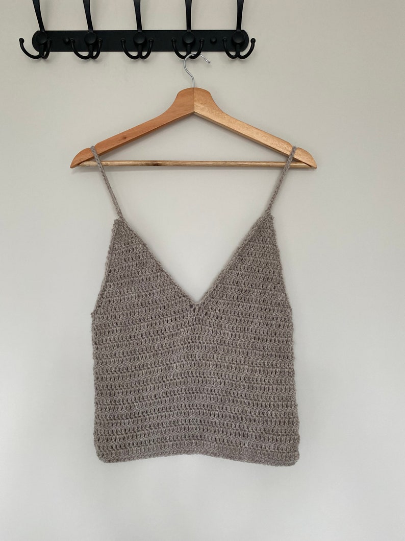 May include: A brown crocheted tank top with a v-neckline hanging on a wooden hanger.