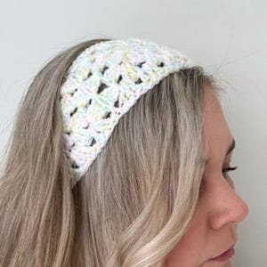 Puede incluir: Una diadema de ganchillo en colores pastel amarillo, rosa y azul. La diadema es blanca con un estampado floral. El accesorio se lleva en la cabeza y está hecho de hilo.