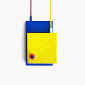 May include: A yellow square with a red button on top, stacked on top of a blue square. Both squares are hanging from a white ceiling.