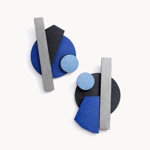 Puede incluir: Dos obras de arte murales abstractas de madera. Cada una presenta una forma rectangular gris, un semicírculo negro, un círculo azul, un semicírculo azul y un triángulo azul. Las obras están sobre un fondo blanco.
