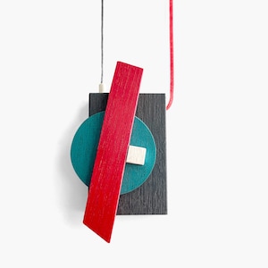May include: A geometric wooden pendant necklace with a red, teal, and black color scheme. The pendant is made of layered wood pieces and hangs from a red cord.