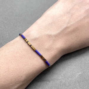 Könnte beinhalten: Ein violettes und goldenes Armband mit quadratischen Perlen.