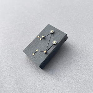 Könnte beinhalten: Ein schwarzes quadratisches Holzstück mit einem Konstellationsdesign. Die Konstellation besteht aus goldenen Punkten und dünnen schwarzen Linien. Die Konstellation ist das Sternbild Waage.