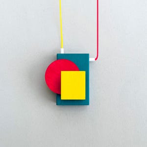 Peut inclure: Pendentif de collier g&eacute;om&eacute;trique abstrait. Il pr&eacute;sente une base rectangulaire turquoise, un cercle rouge et un carr&eacute; jaune. Le collier a un cordon jaune et rouge, et des connecteurs blancs. Le design est moderne et color&eacute;.