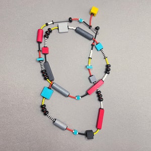 May include: A colorful necklace with black, red, blue, yellow, and gray wooden beads and geometric shapes. The necklace is made of a variety of materials, including wood, metal, and plastic.