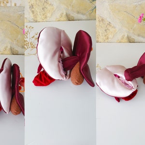 May include: A plush toy shaped like a heart with a burgundy exterior and a pink interior. The heart is open and the interior is visible. The toy is made of soft fabric and has a three-dimensional shape.