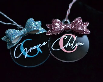 Peut inclure: Deux décorations de Noël personnalisées avec des nœuds pailletés. Un ornement est bleu avec le nom "Grace" et l'autre est rose avec le nom "Chloe".