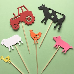 May include: A set of six farm animal themed cake toppers. The toppers are made of paper and feature a red tractor, a black and white cow, a white sheep, an orange chicken, a pink pig, and a yellow duck. The toppers are attached to wooden skewers.