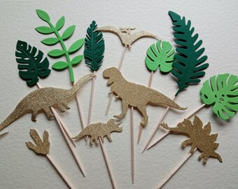 Puede incluir: Un conjunto de 10 adornos para tartas de dinosaurio y hojas tropicales de purpurina dorada. Los adornos están hechos de papel y tienen un acabado brillante. Son perfectos para una fiesta con temática de dinosaurios.