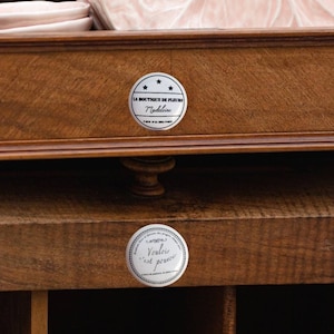 Puede incluir: Un cajón de madera con dos pegatinas plateadas. La pegatina superior dice "La Boutique de Fleurs Madeleine". La pegatina inferior dice "Vinyle et papier".