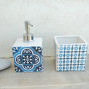May include: A square ceramic soap dispenser with a blue and white floral tile pattern and a silver pump, paired with a matching square open-top container featuring a blue and white geometric grid pattern on its exterior surfaces.