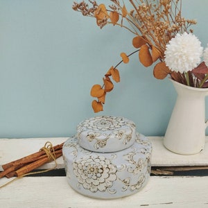 Könnte beinhalten: Eine zweistufige Keramikdose mit einem floralen Design in Blau- und Brauntönen. Die Dose hat einen Deckel und ist mit komplizierten Mustern verziert.