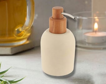 May include: A cream-colored soap dispenser with a cylindrical wooden pump mechanism and a silver-toned metal nozzle. The base of the dispenser is rounded and smooth, featuring a matte finish that contrasts with the natural wood grain of the top.