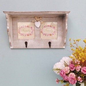 May include: White wooden shelf with two hooks and two framed pictures that say "Family" in a floral design. A white heart is hanging from the top of the shelf.
