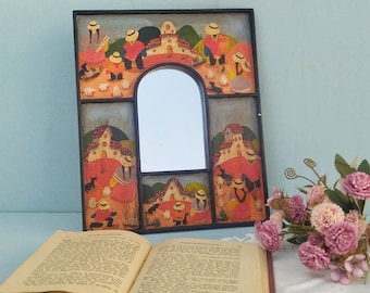 May include: A rectangular mirror with a black frame featuring hand-painted scenes of people in straw hats, small houses, and animals. The painted panels surround a central arched mirror glass. The artwork uses a palette of red, green, and yellow.
