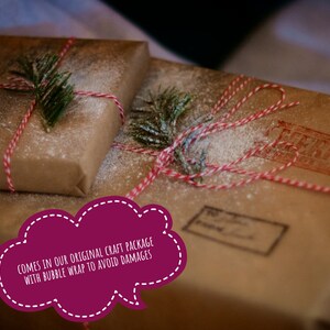 May include: Two rectangular packages wrapped in brown craft paper, tied with red and white baker's twine, and decorated with small green pine sprigs. The packages are dusted with white powder and feature a red ink stamp and a shipping label.