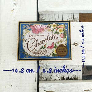 May include: A vintage tin box with a blue background and gold trim. The box features a floral design with butterflies and the text "DELICIOUS - Chocolates - QUALITY GUARANTEED". The box measures 5.8 inches by 4.4 inches.