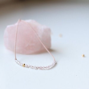 Könnte beinhalten: Eine zarte rosa und goldene Halskette mit kleinen, facettierten Perlen. Die Halskette ist aus Rosenquarz und goldenen Perlen gefertigt.
