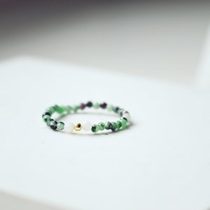 Könnte beinhalten: Ein zarter Ring aus grünen, rosa und weißen Perlen mit einem goldenen Akzent.