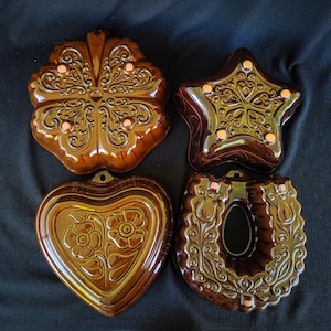 Könnte beinhalten: Vier braune Keramikformen in verschiedenen Formen: ein vierblättriges Kleeblatt, ein Stern, ein Herz mit floralen Details und ein Ring mit einer zentralen Öffnung. Jede Form hat aufwendige geprägte Designs und kleine, runde Akzente.