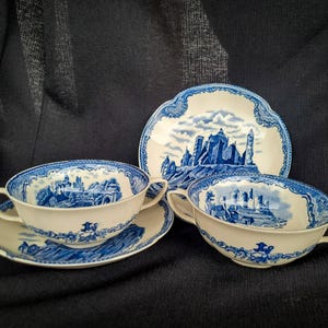 Puede incluir: Un juego de vajilla de porcelana azul y blanca vintage. El juego incluye dos tazas de sopa con asas y platillos a juego, y un plato decorativo. Cada pieza presenta un diseño de paisaje.