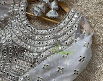 May include: A silver and white embroidered blouse with a sheer fabric and a round neckline. The blouse is decorated with small mirrors and sequins.