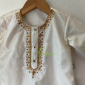 May include: White kurta with gold and green embroidery. The neckline and front of the garment are adorned with intricate embellishments.