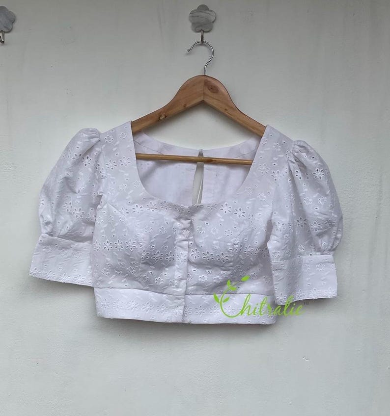 May include: White cotton blouse with a round neckline and short puffed sleeves. The blouse has a button-up front and is decorated with eyelet embroidery.