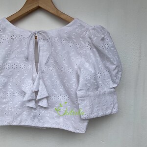 May include: White eyelet crop top with a tie back and puff sleeves. The top features a delicate floral pattern.