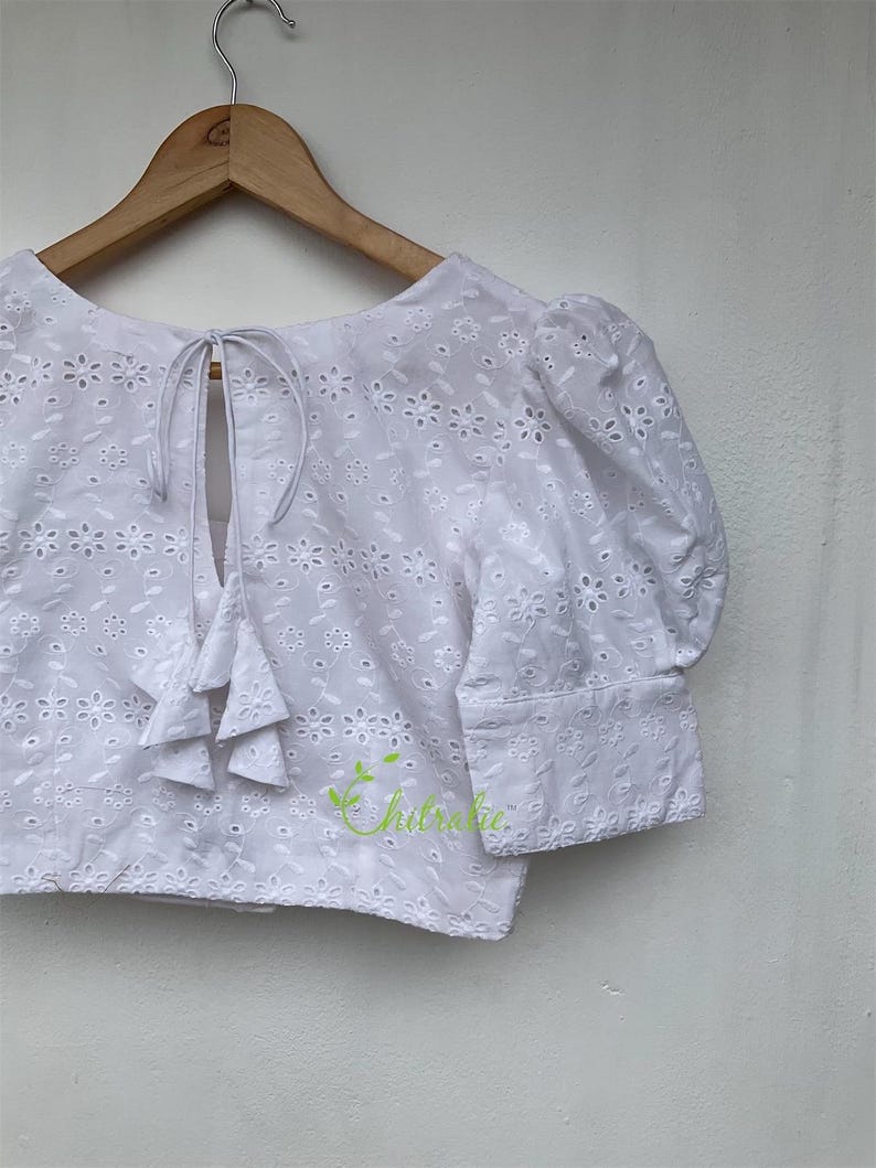 May include: White eyelet crop top with a tie back and puff sleeves. The top features a delicate floral pattern.