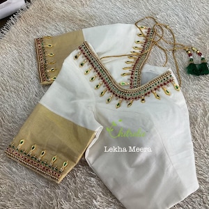 May include: White blouse with gold and red embroidered detailing around the neckline and sleeve cuffs. The sleeves are a contrasting gold color. The blouse has the text "Chitrula Lekha Meera" in green.