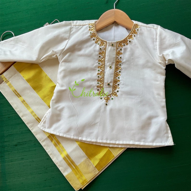 May include: White long-sleeved shirt with gold and green embroidery. The shirt is paired with a white and gold dhoti.
