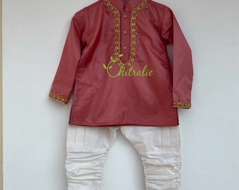 May include: A pink kurta with gold embroidery and white pants. The kurta has a mandarin collar and long sleeves. The pants are pleated and have a loose fit.