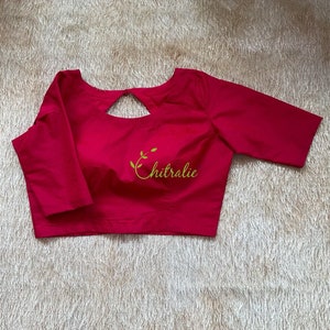 May include: A bright pink, short-sleeved blouse with a keyhole cutout in the back. The blouse has a small embroidered logo that says "Chitralie".